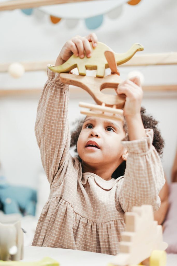 Adorable child with curly hair enjoys playing with wooden toys indoors. Capturing innocent joy and playfulness.